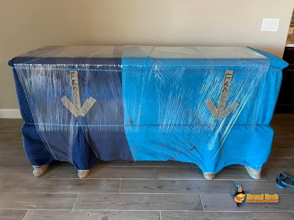 A dresser fully wrapped in moving blankets, marked fragile, by Round Rock Affordable Movers