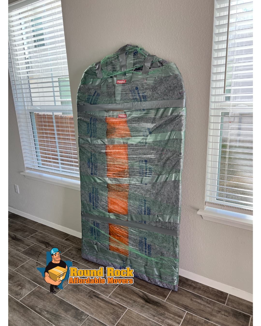 A large mirror fully wrapped in moving blankets and tape, marked fragile, by Round Rock Affordable Movers